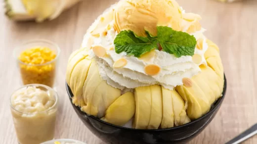 Mangkuk penuh es durian yang lezat, disajikan dengan irisan durian segar dan daun mint sebagai hiasan, siap dinikmati di hari yang panas