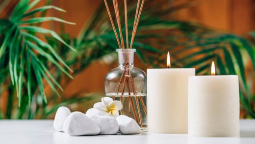 Lilin aromaterapi dengan aroma lavender diletakkan di atas meja kayu, menyala dengan lembut di ruang tamu yang diterangi cahaya remang, menciptakan suasana yang tenang dan santai
